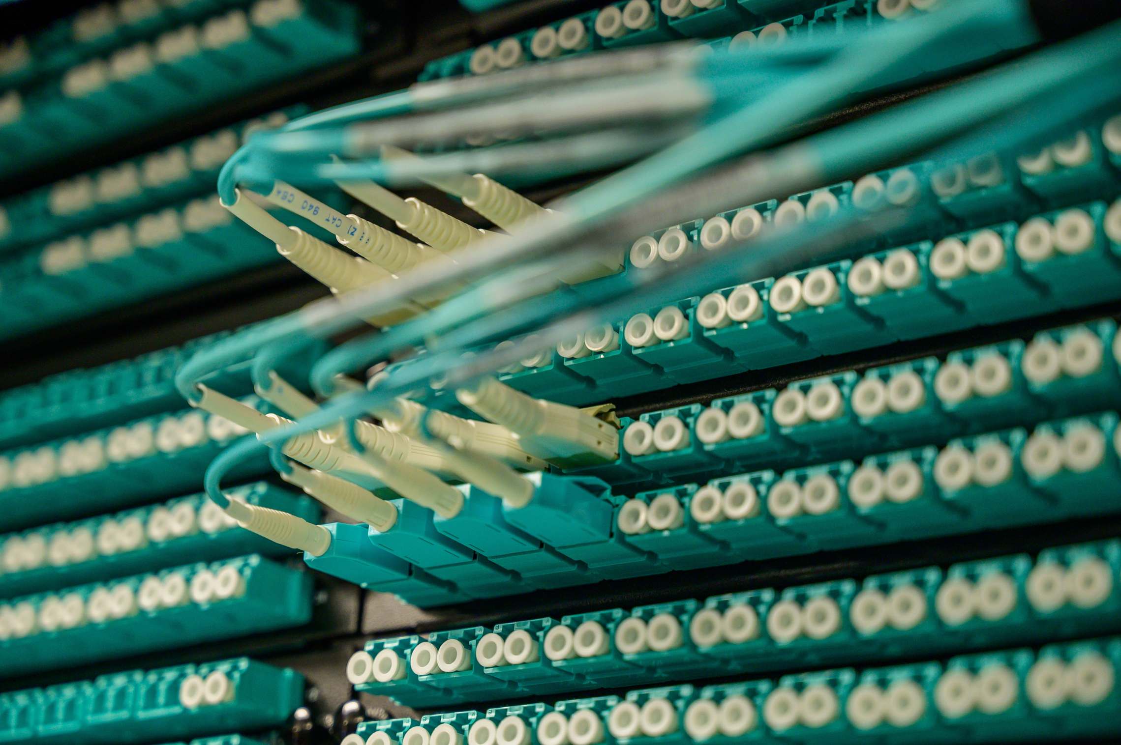 Rows of server racks in a data hall with fiber optic cables connected